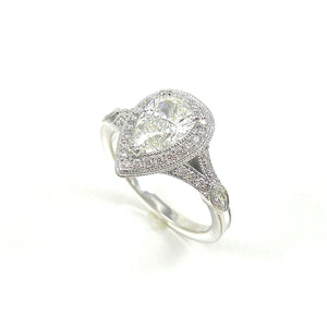 handcrafted halo engagement ring featuring a pear shaped center stone with round brilliant diamond and milgrain accents