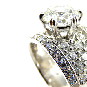 close up of round brilliant cut diamond center stone ring with a pave diamond accented shank and diamond borders